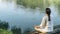 Yoga Retreat. Peaceful Young Woman Sitting in Lotus Position and Meditating by the Lake