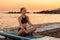 Yoga sup board. Young slim woman meditates on a surf board. In the background, the ocean, the horizon and the sunset