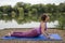 Yoga teacher demonstrates the cobra pose beside a lake