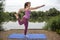 Yoga teacher demonstrates the Dancer pose beside a lake