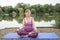 Yoga teacher demonstrates the Half Lotus pose beside a lake