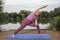 Yoga teacher demonstrates the Side Angle Bend pose beside a lake