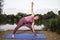 Yoga teacher demonstrates the Triangle pose beside a lake