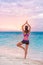 Yoga wellness class on beach at sunset. Girl practicing meditation standing on one leg training balance barefoot on sand