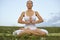 Yoga woman meditation in nature. Athletic woman in white clothes meditates in lotus position on the grass in summer