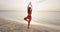 Yoga woman poses at beach doing yoga tree pose at sunrise