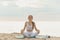 Yogini girl performs breathing practice sitting in the lotus position on the seashore at dawn. Young woman practicing yoga at the