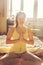 Yogini woman boho woman with mala necklace meditating in lotus asana in sunny room