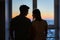 Yong couple in love standing close to window during the sunrise, silhouette medium shoot.