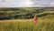 Yong woman with long hair in red dress walking in summer field with tall green grass on rural hill environment.