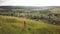 Yong woman with long hair in red dress walking in summer field with tall green grass on rural hill environment.