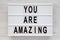 `You are amazing` words on a lightbox on a white wooden background, top view. Overhead, from above. Flat lay. Close-up