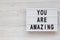 `You are amazing` words on a modern board on a white wooden background, top view. Overhead, from above. Flat lay. Space for text