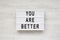 `You are better` words on a lightbox over white wooden background, top view. Overhead, from above. Flat lay