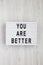 `You are better` words on a lightbox over white wooden surface, top view. Overhead, from above. Flat lay