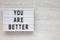 `You are better` words on a lightbox on a white wooden background, top view. Overhead, from above. Flat lay. Copy space