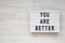 `You are better` words on a lightbox on a white wooden background, top view. Overhead, from above. Flat lay. Copy space