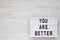 `You are better` words on a lightbox on a white wooden surface, top view. Overhead, from above. Flat lay. Space for text