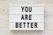 `You are better` words on a modern board over white wooden background, top view. Overhead, from above. Flat lay