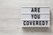 `Are you covered?` words on a modern board on a white wooden background, top view. Overhead, from above, flat lay. Copy space