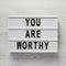 `You are worthy` on a lightbox on a white wooden background, top view. Flat lay, overhead, from above
