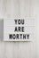 `You are worthy` on a lightbox on a white wooden surface, top view. Flat lay, overhead, from above