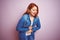 Youg beautiful redhead woman wearing denim shirt standing over isolated pink background with hand on stomach because indigestion,