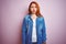 Youg beautiful redhead woman wearing denim shirt standing over isolated pink background puffing cheeks with funny face