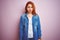 Youg beautiful redhead woman wearing denim shirt standing over isolated pink background skeptic and nervous, frowning upset