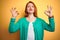 Youg beautiful redhead woman wearing winter green sweater over isolated yellow background relax and smiling with eyes closed doing