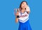 Youn beautiful asian girl wearing cheerleader uniform holding champion trophy with open hand doing stop sign with serious and