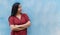 Young 20 year old Latina standing with arms crossed on blue wall background