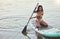 Young active african female smiling and kneeling on her paddle board on a lake out in nature. Young female enjoying a