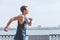 Young active athlete muscular Male dressed sleeveless shirt running by the river promenade on the sunny day. Man enjoying a