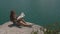 Young active backpacker girl rests on mountain rock upon large water surface of mountain lake and looking to map