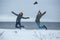 Young active couple joyful jumping up high together on winter holiday beach, nature outdoors. Fun energy recreational