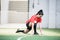 Young active female footballer in sports uniform doing exercise for stretching