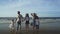 Young active parents with three daughters enjoying barefoot in water on beach.