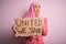 Young activist woman wearing pink muslim hijab holding banner with united we stand message serious face thinking about question,