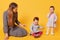 Young adorable caring mother looks after her little kids, sitting on floor with one of twin girls. Sweet child puts one hand on