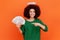 Young adult angelic woman with curly hair wearing green casual style sweater with nimb over head holding and pointing at fan of