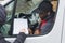 Young adult black delivery guy sitting in driver seat of white van leaning out of window to check papers signed by