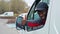 Young adult black delivery man wearing black cap driving white van leaning out the window to look behind.