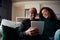 Young adult couple, multi-ethnic, sitting on sofa in modern apartment using tablet