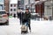 Young adult father pushing baby stroller and walking on snow covered sidewalk at town after blizzard