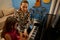 Young adult female pianist, music teacher teaching piano and music lesson to a little girl in elegant red dress, sitting