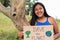 Young adult girl holds up a poster calling for saving the planet while hugging a tree. Portrait of brunette woman on a