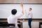 Young adult male student raising hands up in the air to ask questions from another male teacher.