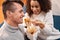 Young adult man and afro american woman sitting on couch, eating chinese fast food