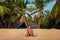 A young adult man sits on the sand of Karon Beach in Thailand on a background of coconut palm trees